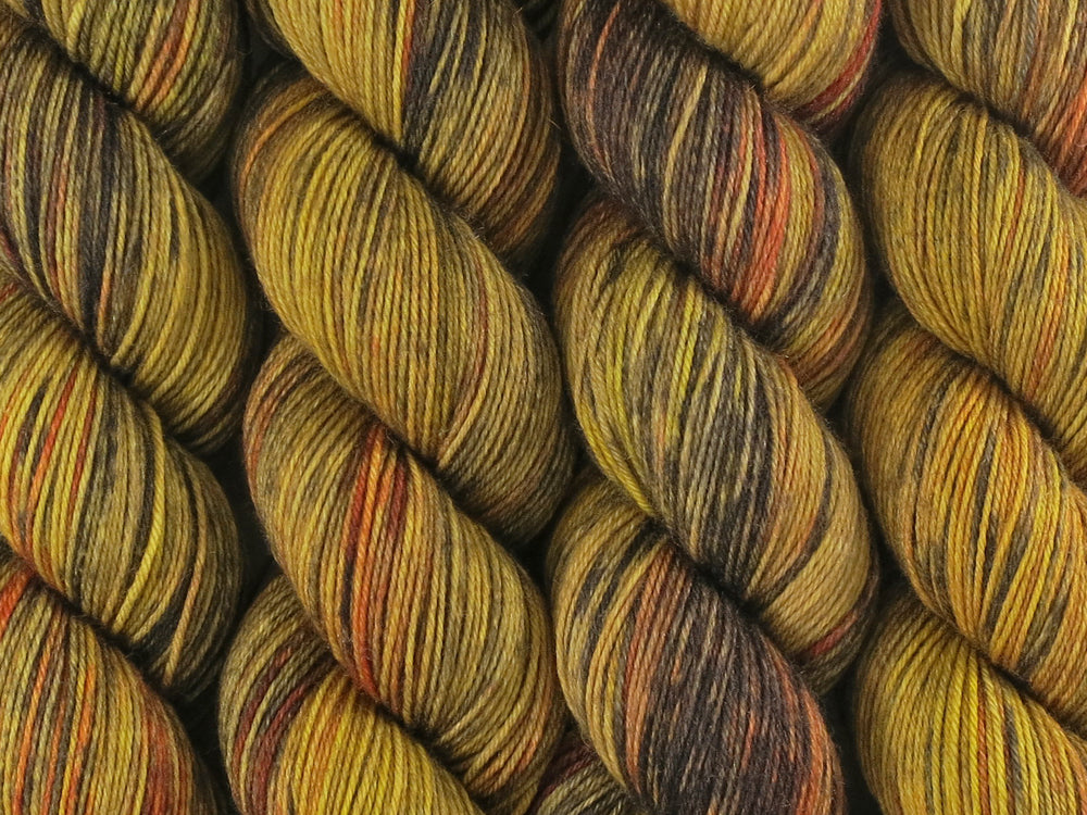 A close up of variegated golden yellow, ebony, honey and rust coloured skeins of superwash merino and nylon 4ply fingering sock yarn (Honeyant on Tough Stocking)