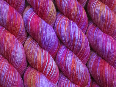 A close up of variegated purples, magenta, orange and yellow coloured skeins of superwash merino and nylon 4ply fingering sock yarn (Hooternanny on Tough Stocking)
