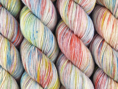 A close up of variegated white, bright yellow, orange, teal and purple coloured skeins of superwash merino and nylon 4ply fingering sock yarn (I'm Going Slightly Mad on Tough Stocking)