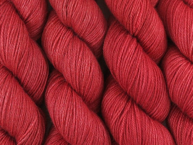 A close up of semi-solid medium red with hints of maroon and crimson coloured skeins of superwash bluefaced leicester, silk and cashmere 4ply fingering sock yarn (Japonica on Blue Chip Stocking)