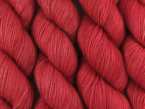 A close up of semi-solid medium red with hints of maroon and crimson coloured skeins of superwash bluefaced leicester, silk and cashmere 4ply fingering sock yarn (Japonica on Blue Chip Stocking)