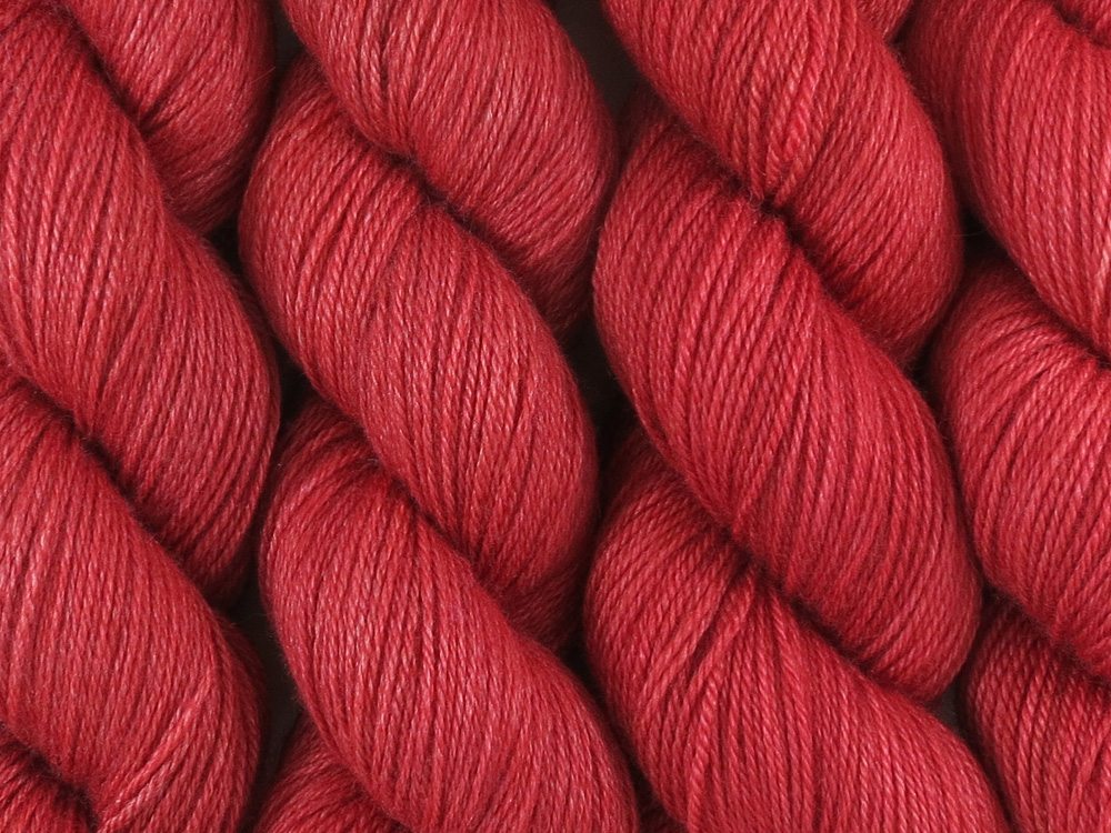 A close up of semi-solid medium red with hints of maroon and crimson coloured skeins of superwash bluefaced leicester, silk and cashmere 4ply fingering sock yarn (Japonica on Blue Chip Stocking)