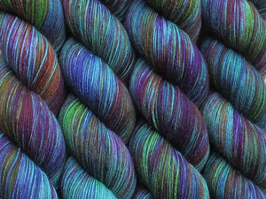 A close up of variegated emerald green, maroon, orange, violet and chartreuse green coloured skeins of superwash merino and nylon 4ply fingering sock yarn (Juggernauts on Tough Stocking)