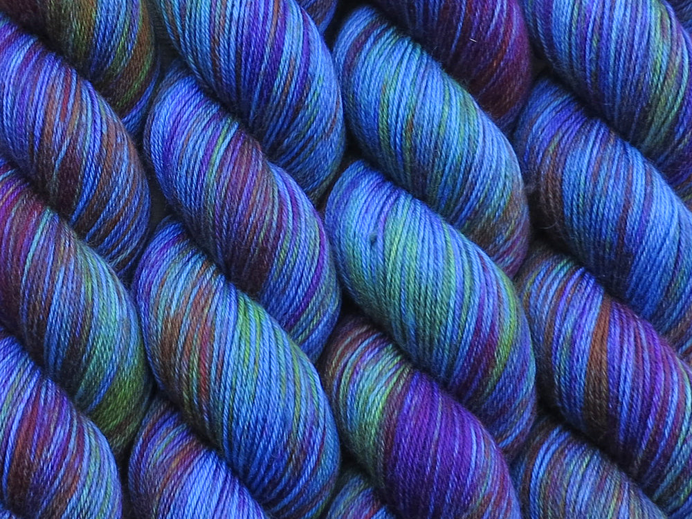 A close up of variegated blues, deep pink, orange, maroon and green coloured skeins of superwash merino and nylon 4ply fingering sock yarn (Lake Tittycaca on Tough Stocking)