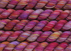 A close up of variegated light grey with hints of yellow, orange, pink and purple mini skeins of superwash merino and nylon 4ply fingering sock yarn arranged horizontally (Lovely Pair Of Coconuts on Tough Stocking Mini)