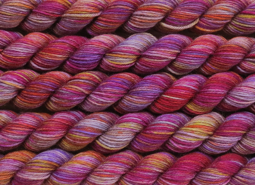 A close up of variegated light grey with hints of yellow, orange, pink and purple mini skeins of superwash merino and nylon 4ply fingering sock yarn arranged horizontally (Lovely Pair Of Coconuts on Tough Stocking Mini)