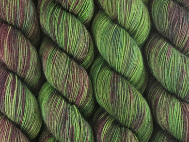 A close up of variegated bright kelly green and maroon with hints of forest and hunter greens, chartreuse and umber coloured skeins of superwash merino and nylon 4ply fingering sock yarn (Mesclun Mix on Tough Stocking)