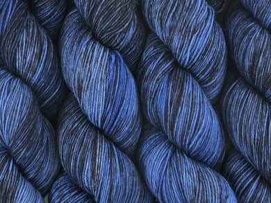 A close up of variegated yarn of black and charcoal with overtones of denim, chambray and navy coloured skeins of superwash merino and nylon 4ply fingering sock yarn (Moody Blues on Tough Stocking)