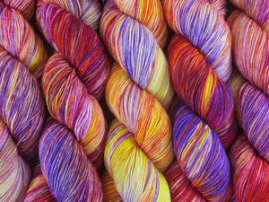 A close up of variegated white, yellow, orange, pink and purple coloured skeins of superwash merino and nylon 4ply fingering sock yarn (Much Ado About Knockers on Tough Stocking)