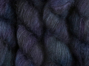 A close up of variegated black with hints of fuchsia, Kelly green and royal blue coloured skeins of superfine kid mohair and silk 2ply lace yarn (Nevermore on Kid Glove Lace)