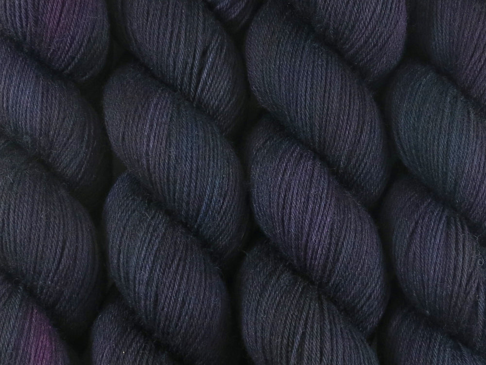 A close up of variegated black with hints of pink, blue and green coloured skeins of superwash merino and nylon 4ply fingering sock yarn (Nevermore on Tough Stocking)
