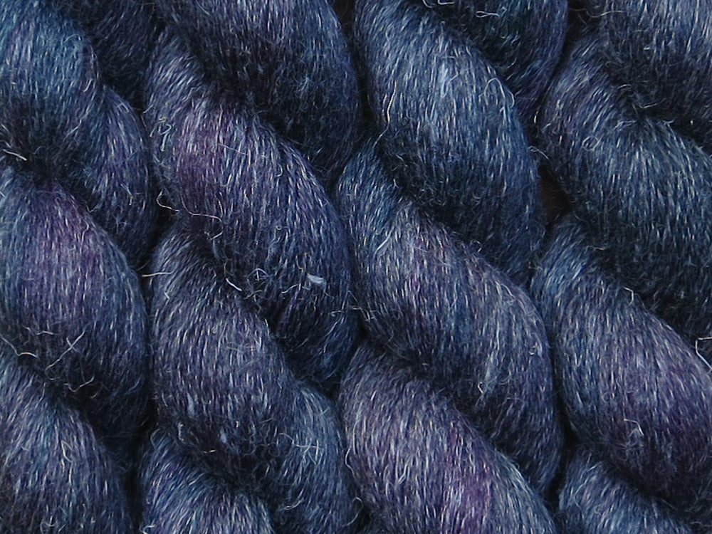 A close up of variegated black with hints of fuchsia, kelly green and royal blue coloured skeins of non-superwash baby alpaca, silk and linen 4ply fingering weight yarn (Nevermore on Spinifex)