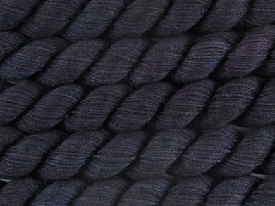A close up of variegated black with hints of fuchsia, kelly green and royal blue mini skeins of superwash merino and nylon 4ply fingering sock yarn arranged horizontally (Nevermore on Tough Stocking Mini)