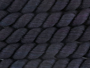 A close up of variegated black with hints of fuchsia, kelly green and royal blue mini skeins of superwash merino and nylon 4ply fingering sock yarn arranged horizontally (Nevermore on Tough Stocking Mini)