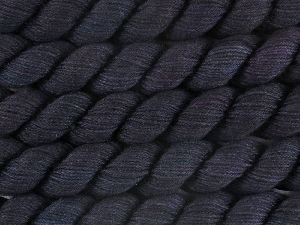 A close up of variegated black with hints of fuchsia, kelly green and royal blue mini skeins of superwash merino and nylon 4ply fingering sock yarn arranged horizontally (Nevermore on Tough Stocking Mini)