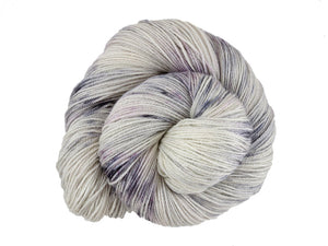 A close up of a white and soft grey with speckles of black and purple coloured skein of superwash bluefaced leicester, silk and cashmere 4ply fingering sock yarn presented as a spiral on a white background (Newsprint on Blue Chip Stocking)