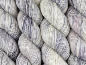A close up of white and soft grey with speckles of black and purple coloured skeins of superwash bluefaced leicester, silk and cashmere 4ply fingering sock yarn (Newsprint on Blue Chip Stocking)
