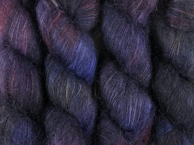 A close up of variegated deep blue, charcoal, violet, blood red and hints of straw yellow coloured skeins of superfine kid mohair and silk 2ply lace yarn (Night's Watch on Kid Glove Lace)