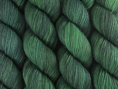 A close up of semi-solid deep green with hints of charcoal, emerald, chartreuse and kelly green coloured skeins of superwash merino and nylon 4ply fingering sock yarn (Nori on Tough Stocking)