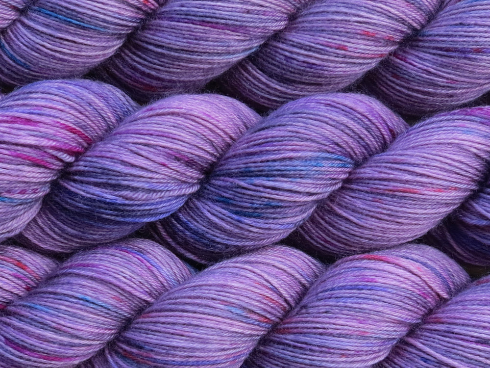 A close up of mauve with speckles of blue, pink and charcoal coloured skeins of superwash merino and nylon 4ply fingering sock yarn (One Hit Wonder 1 on Tough Stocking)