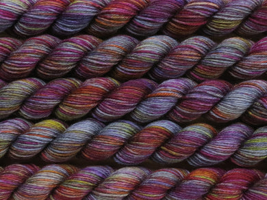 A close up of variegated blue grey with hints of yellow, orange, pink and purple mini skeins of superwash merino and nylon 4ply fingering sock yarn arranged horizontally (Over The Shoulder Boulder Holder on Tough Stocking Mini)
