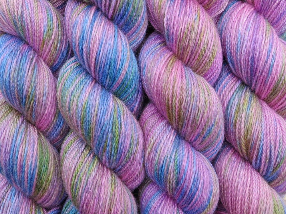 A close up of variegated light bright pink, blue, green and mauve coloured skeins of superwash bluefaced leicester, silk and cashmere 4ply fingering sock yarn (Pinkapalooza on Blue Chip Stocking)