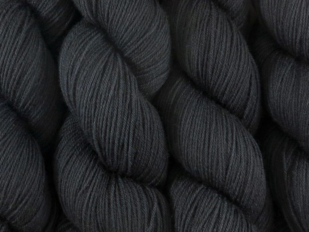 A close up of almost solid black coloured skeins of superwash merino and nylon 4ply fingering sock yarn (Pitch Black on Tough Stocking)