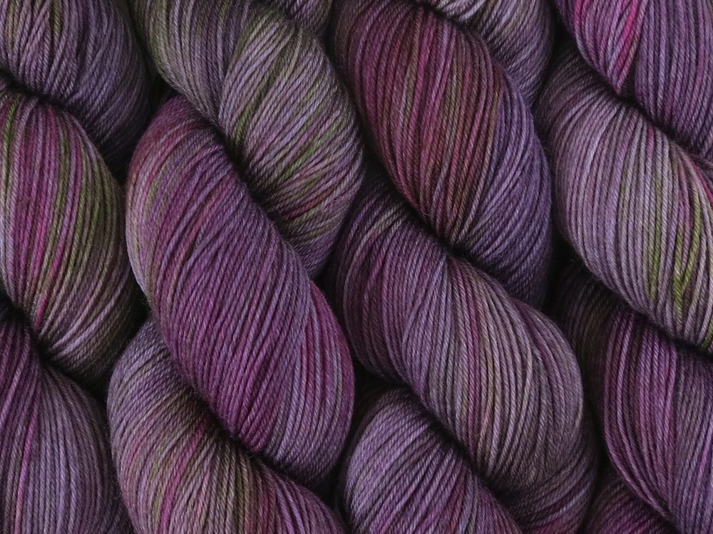 A close up of variegated purple, violet and green with hints of hot pink and beige coloured skeins of superwash merino and nylon 4ply fingering sock yarn (Purple Sea Urchin on Tough Stocking)
