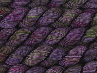 A close up of variegated purple, violet and green with hints of hot pink and beige mini skeins of superwash merino and nylon 4ply fingering sock yarn arranged horizontally (Purple Sea Urchin on Tough Stocking Mini)