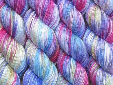 A variegated blues, magenta, white and yellow green coloured skeins of superwash merino and silk 4ply fingering sock yarn (Rhelma on Silk Stocking)
