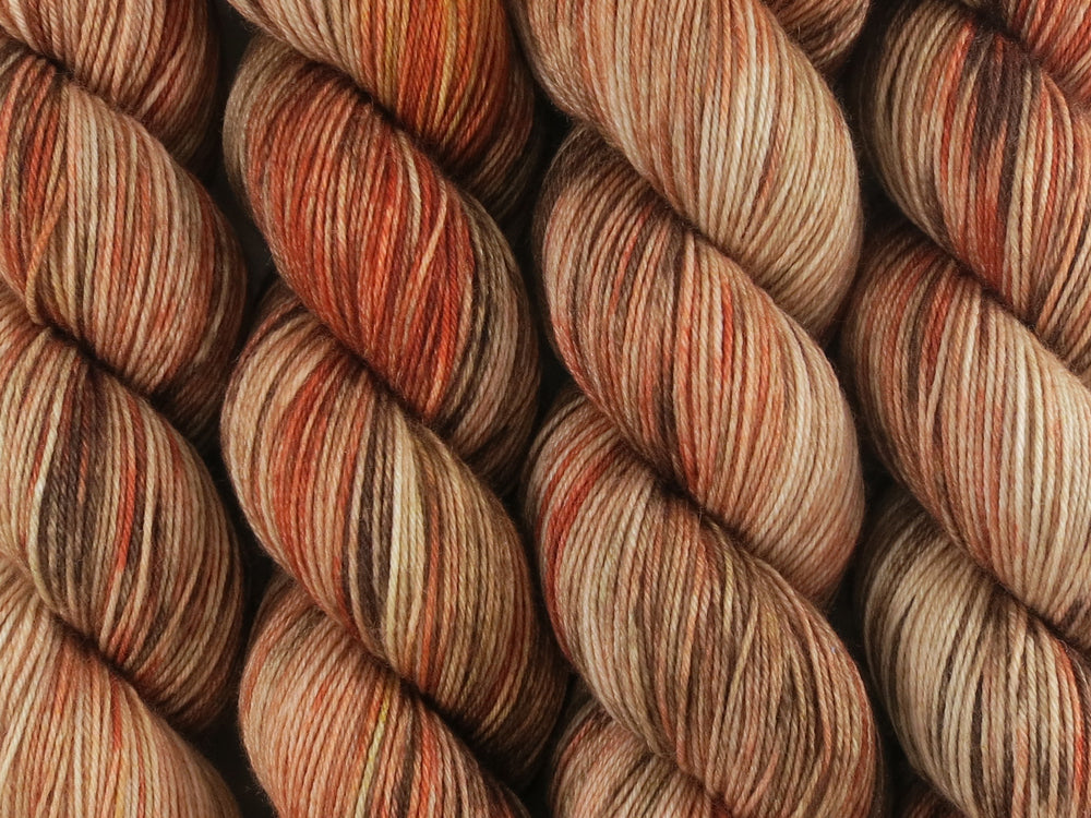 A close up of variegated rust, chocolate, tan and beige coloured skeins of superwash merino and nylon 4ply fingering sock yarn (River Red Gum on Tough Stocking)