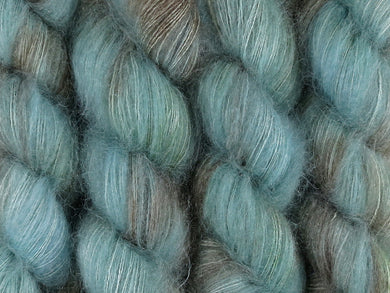 A close up of variegated blue, aqua, brown with hints of kelly green coloured skeins of superfine kid mohair and silk 2ply lace yarn (Rockpool on Kid Glove Lace)