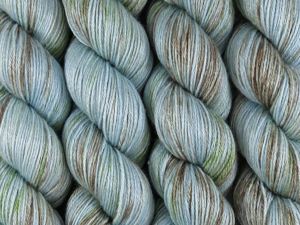 A close up of variegated blue, aqua and brown with hints of kelly green coloured skeins of superwash merino and silk 4ply fingering sock yarn (Rockpool on Silk Stocking)