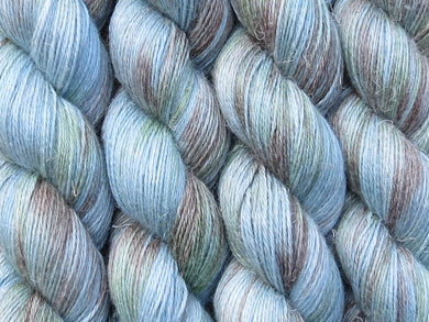 A close up of variegated pale blue with hints of aqua, brown and green coloured skeins of non-superwash baby alpaca, silk and linen 4ply fingering weight yarn (Rockpool on Spinifex)