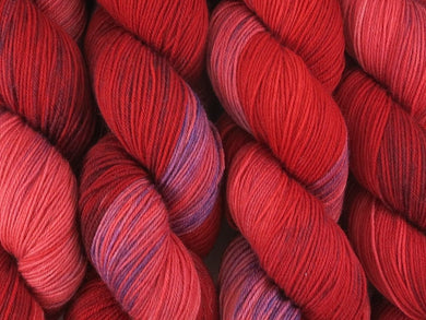 A close up of variegated red and light pink with hints of purple coloured skeins of superwash merino and nylon 4ply fingering sock yarn (Rosella  on Tough Stocking)