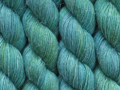 A close up of variegated light grey-green with hints of pink, sulphur yellow and deep jade green coloured skeins of non-superwash baby alpaca, silk and linen 4ply fingering weight yarn (Samphire on Spinifex)