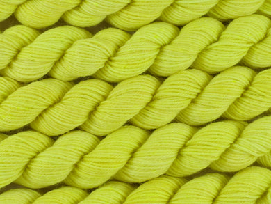 A close up of semi-solid light bright lemon yellow with hints of neon yellow and gold mini skeins of superwash merino and nylon 4ply fingering sock yarn arranged horizontally (Sherbet Lemon on Tough Stocking Mini)