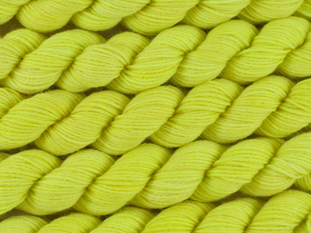 A close up of semi-solid light bright lemon yellow with hints of neon yellow and gold mini skeins of superwash merino and nylon 4ply fingering sock yarn arranged horizontally (Sherbet Lemon on Tough Stocking Mini)