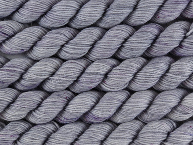 A close up of tonal silver grey with speckles of pink and purple mini skeins of superwash merino and nylon 4ply fingering sock yarn arranged horizontally (Silver Screen on Tough Stocking Mini)