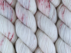 A close up of white, grey and soft brown with speckles of red coloured skeins of superwash merino and nylon 4ply fingering sock yarn (Six White Boomers on Tough Stocking) Edit alt text