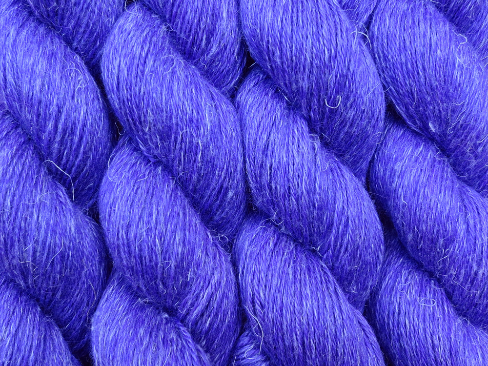 A close up of semi-solid deep purple with undertones of fuchsia coloured skeins of non-superwash baby alpaca, silk and linen 4ply fingering weight yarn (Snozzberries on Spinifex)