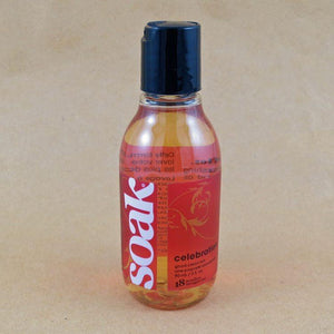 One small bottle of Soak rinse-free laundry liquid with a dark pink label, on a tan background (Celebration scent)