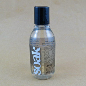 One small bottle of Soak rinse-free laundry liquid with a grey label, on a tan background (Lacey scent)