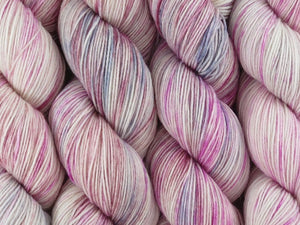 A close up of variegated white, pink, grey, silver and maroon coloured skeins of superwash merino and nylon 4ply fingering sock yarn (Steel Magnolia on Tough Stocking)