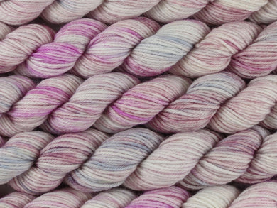 A close up of variegated cool pink and white with hints of grey, silver and maroon mini skeins of superwash merino and nylon 4ply fingering sock yarn arranged horizontally (Steel Magnolia on Tough Stocking Mini)