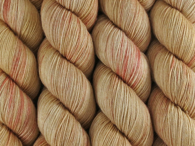 A close up of variegated warm beige tan with coral pink coloured skeins of superwash merino and nylon 4ply fingering sock yarn (Sunburnt on Tough Stocking)
