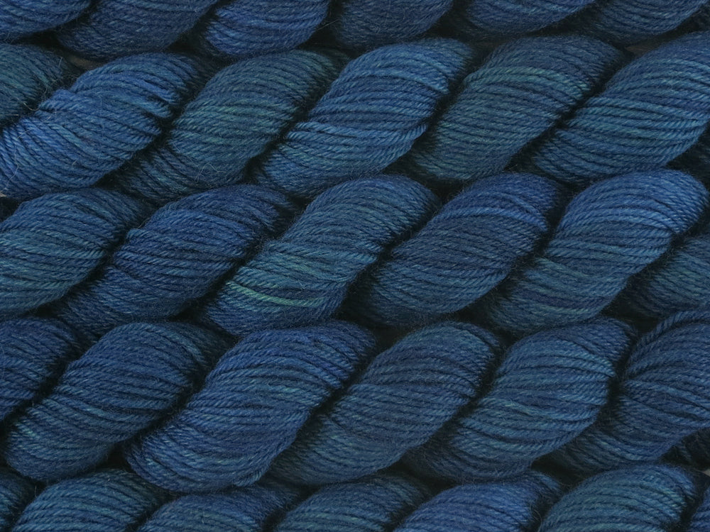 A close up of deep semi-solid blue green, teal and navy with hints of emerald green mini skeins of superwash merino and nylon 4ply fingering sock yarn arranged horizontally (The Kraken Wakes on Tough Stocking Mini)