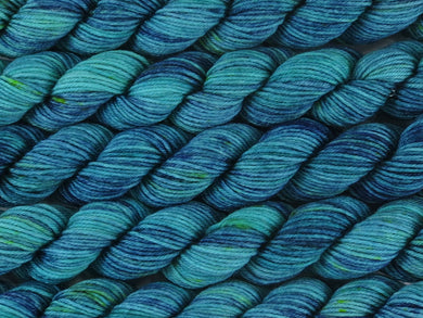 A close up of variegated teal greens and navy blue with speckles of bright yellow mini skeins of superwash merino and nylon 4ply fingering sock yarn arranged horizontally (The Other Woman on Tough Stocking Mini)