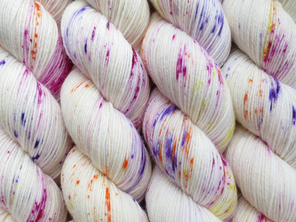 A close up of white with bright speckles of pink, purple, orange and yellow coloured skeins of superwash merino and nylon 4ply fingering sock yarn (Titillation on Tough Stocking)