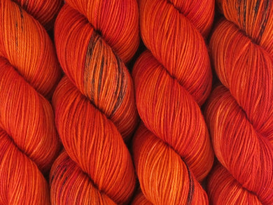 A close up of variegated bright orange, red and fuchsia with black speckles coloured skeins of superwash merino and nylon 4ply fingering sock yarn (Total Fire Ban on Tough Stocking)